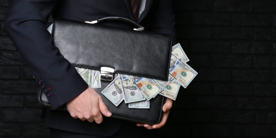 A person in a business suit clutches a briefcase of money