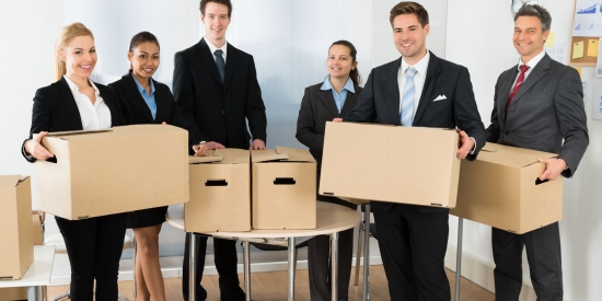 A group of six smiling employees hold cardboard boxes