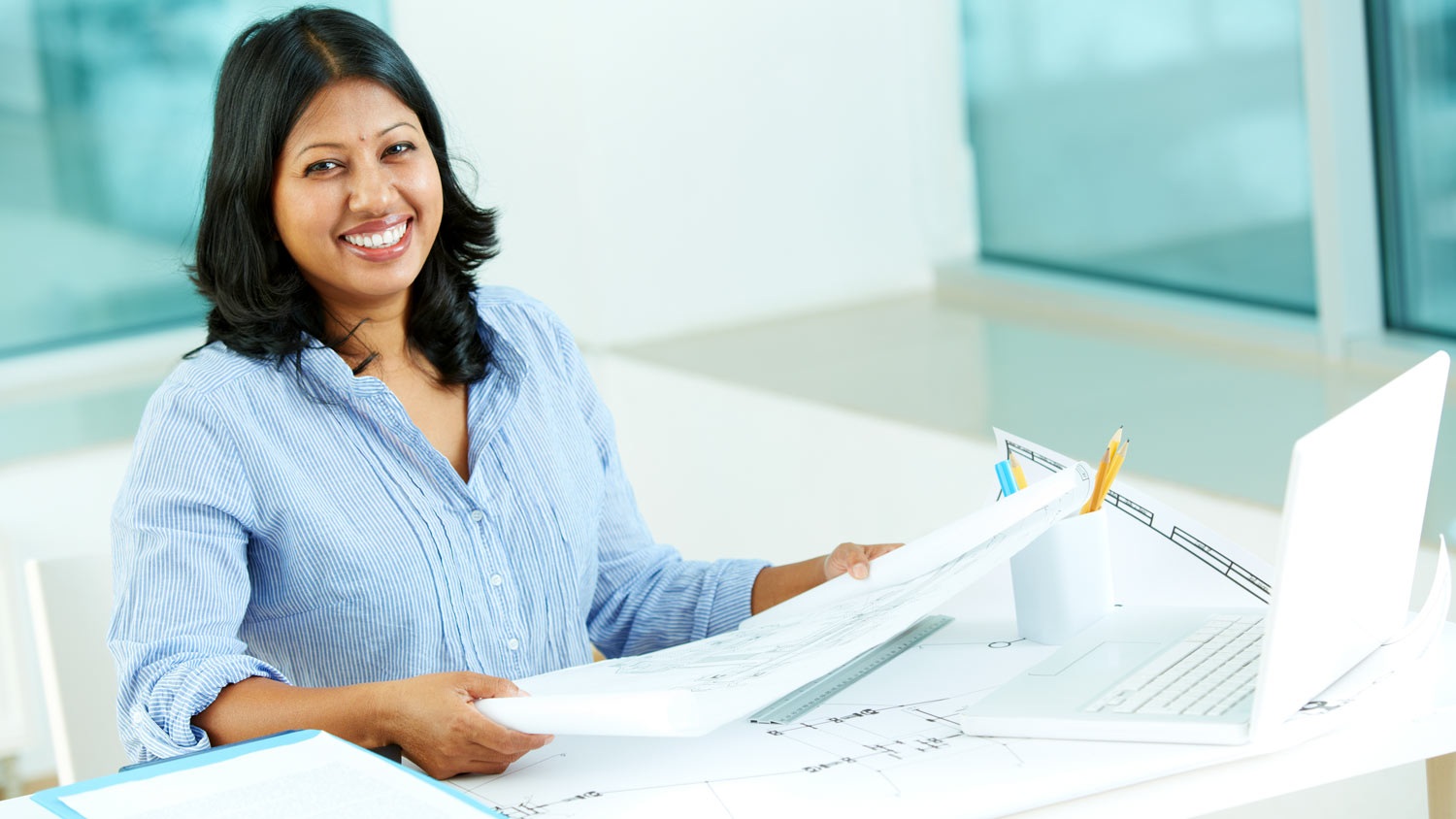 A woman smiles at the camera while holding architectural renderings
