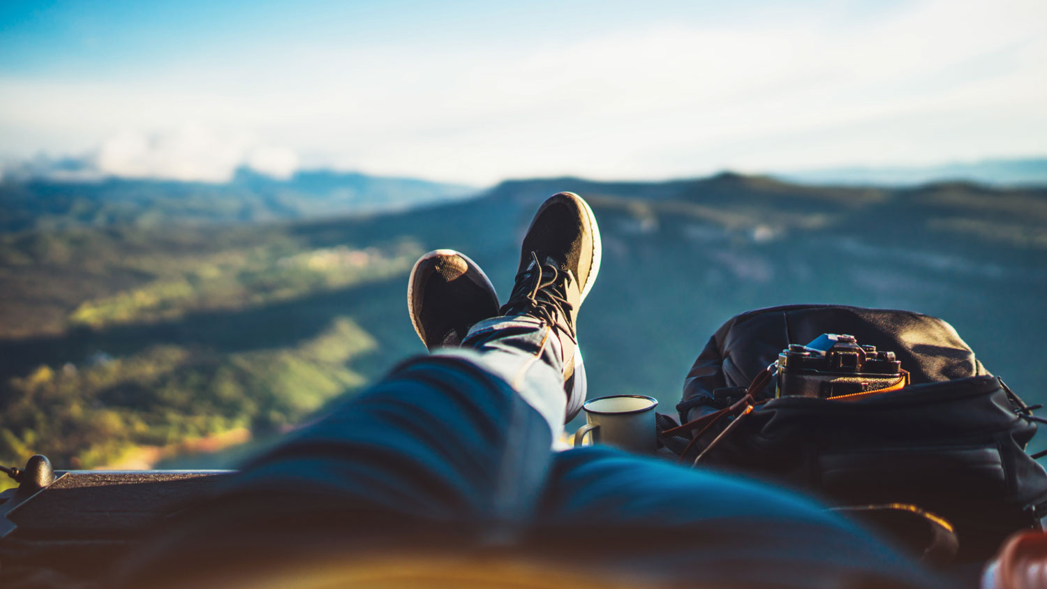 POV photo: legs and hiking boots stretch out in front of a mountainous landscape